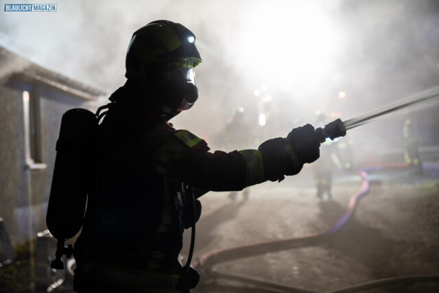 Silhouette einer Einsatzkraft mit Atemschutzgerät in dichtem Rauch bei Nacht