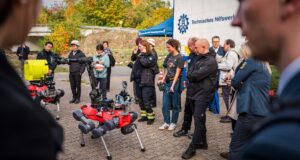 Roboter, Sensoren, Ortung ohne GPS: THW-geführtes EU-Projekt SYNERGISE zeigt Ergebnisse in Berlin Zwei rote vierbeinige Roboter mit Kameras und Greifarm, umringt von Besuchern und Einsatzkräften, im Hintergrund ein THW-Zelt.