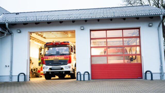 Feuerwehrgerätehaus mit geöffnetem Tor, in dem ein rotes Löschfahrzeug steht.