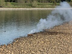 Neuss: Niedrigwasser legt Phosphor-Brandbombe am Rhein frei – Feuerwehr lässt kontrolliert ausbrennen Stark korrodierter zylindrischer Metallkörper am kiesigen Rheinufer, aus dem dichter weißer Rauch aufsteigt; gegenüberliegendes Ufer mit Bäumen.
